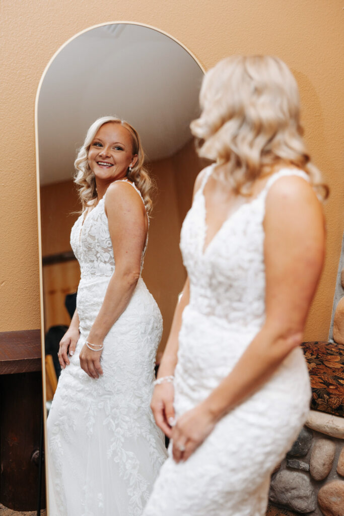 bride in a lace mermaid A line wedding gown smilies at her reflection in a full length mirror