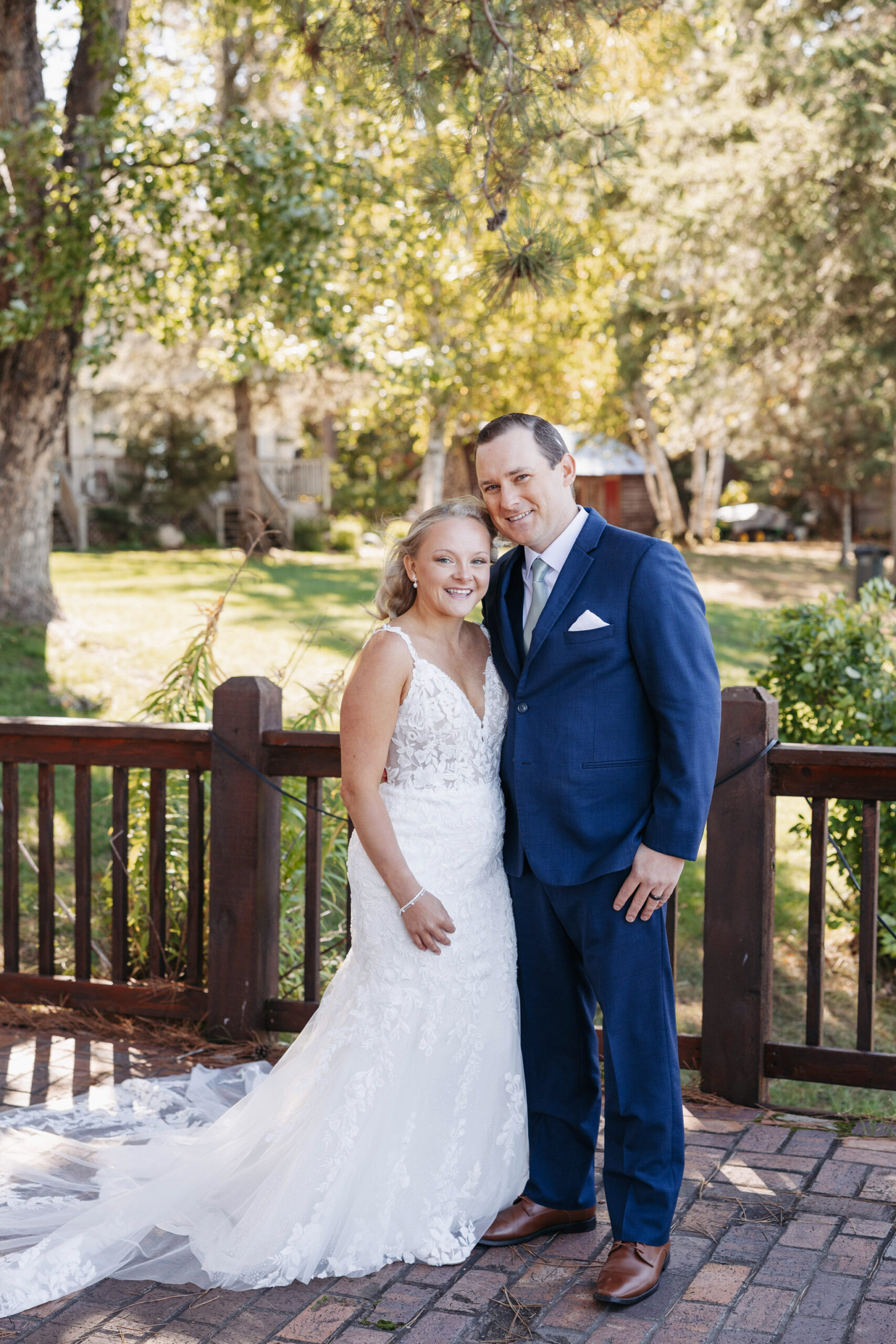 bride and groom pose for the camera side by side on a wooden deck with pine trees in the background during the fall months in Minnesota