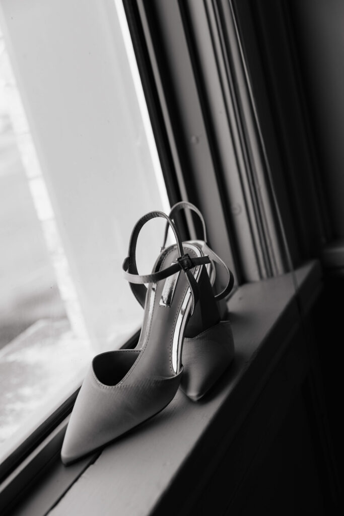 black and white photo of a pair of silk high heels artfully positioned on a windowsill 