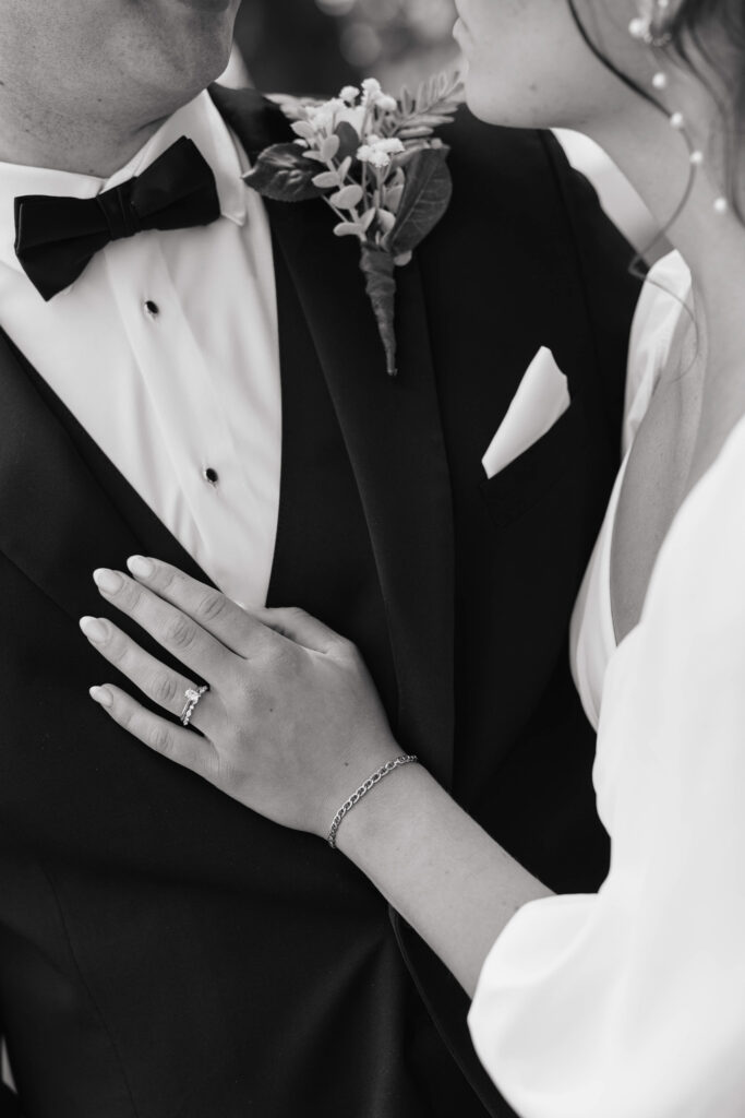 an elegant black and white portrait of a brides hand gently resting on her grooms chest as he wears a bowtie and black tuxedo