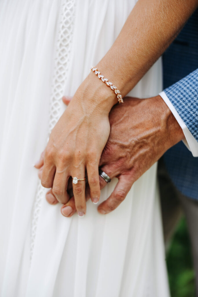 close up short of a bride and groom holding hands a top of the brides dress